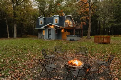 a cabin with chairs and a fire in front of it at Rivers Ledge Cabin with Sauna and Hot Tub in Barryville