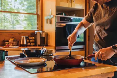 a man cooking food in a bowl on a stove at Breathtaking River Views The Hawks Nest Cabin in Glen Spey