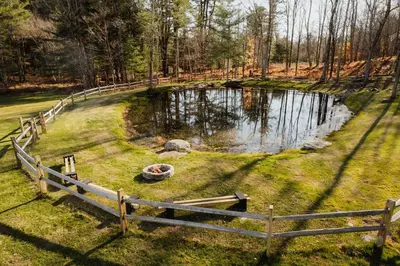 a pond in the middle of a field with a wooden fence at Swan Pond Cabin Hot Tub & Firepit Retreat in Swan Lake