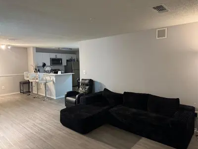 a living room with a black couch and a kitchen at A private master room in modern complex shared apartment in Lawrenceville