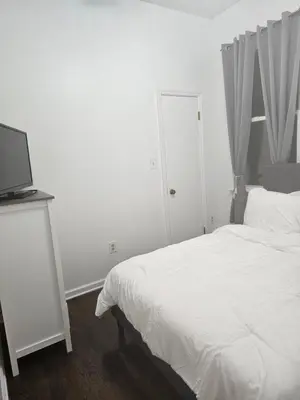 a white bedroom with a bed and a television at Cozy Getaway 3-Prudential Center, NJPAC, Penn Station in Kearny
