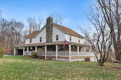 a white house with a chimney and an american flag at Cozy Farmhouse - Fireplace, Backyard, BBQ, Games - 3 MIN TO CAMELBACK in Tannersville