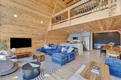 a living room with blue couches and a kitchen at Lakefront AFrame, Heated Pool, Spa, Sauna, Theatre in Blakeslee