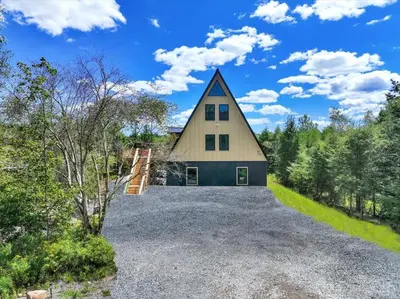 a large house with a gambrel roof on a gravel driveway at Lakefront AFrame, Heated Pool, Spa, Sauna, Theatre in Blakeslee