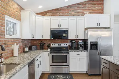 a kitchen with white cabinets and a brick wall at The Rock Oak Escape in Dingmans Ferry