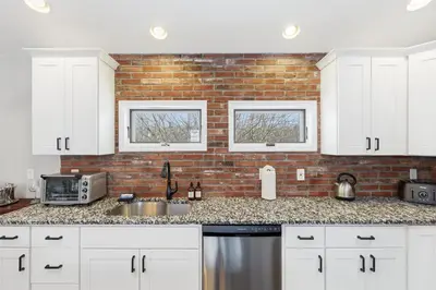 a kitchen with white cabinets and a brick wall at The Rock Oak Escape in Dingmans Ferry