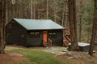a small cabin with an orange door in the woods at Creekside Modern Cabin Sauna Hot Tub Niksen Den in Callicoon