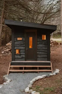 a small cabin with a black door in the woods at Creekside Modern Cabin Sauna Hot Tub Niksen Den in Callicoon