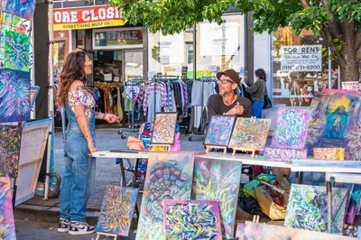 two women standing in a street market with paintings at Family-Friendly 2BR, NYC Access in Minutes in Hoboken