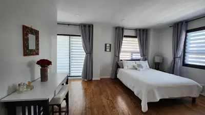 a bedroom with a bed and a desk and windows at Luxury Floral Loft with Balcony Near MetLife & NYC in Bogota
