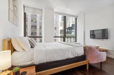 a bedroom with a bed and a tv and windows at FiDi Studio w Work Setup by Anyplace - 10250 in New York