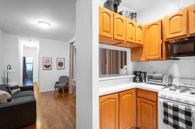 a kitchen with wooden cabinets and a living room at 2-Bedroom Apartment in Hells Kitchen - Manhattan! in New York