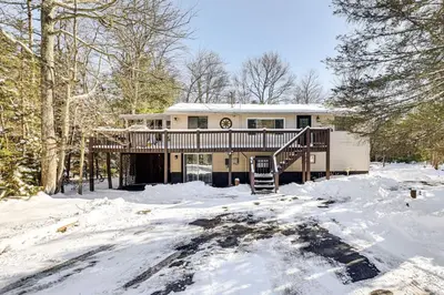 a house with a deck in the snow at Games, Fire Pit, Hot Tub Pocono Lake Family Home! in Pocono Lake