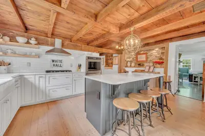 a kitchen with white cabinets and wooden ceilings at Historic Winery Farmhouse by Lake in Hawley