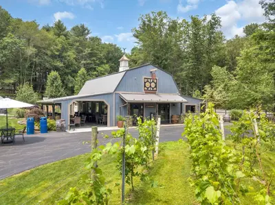 a building in a park with trees in the background at Historic Winery Farmhouse by Lake in Hawley