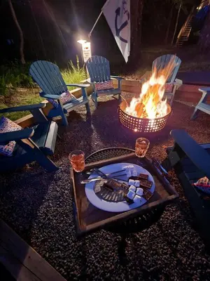 a fire pit with chairs and a table with a plate at Lakefront Hot Tub Canoes Game Room Wood FP in Gouldsboro