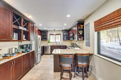 a kitchen with wooden cabinets and a counter with bar stools at Lake Naomi Luxury Home with Stream Pool and Fire Pit in Pocono Pines