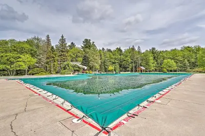 a large swimming pool with a green at Lake Naomi Luxury Home with Stream Pool and Fire Pit in Pocono Pines