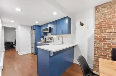 a kitchen with blue cabinets and a brick wall at New Cozy Must Have Stay! 10 minutes to NYC in Hoboken