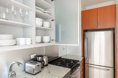 a kitchen with a stainless steel refrigerator and white cabinets at Midtown 1BR w Gym Doorman nr Grand Central NYC-746 in New York