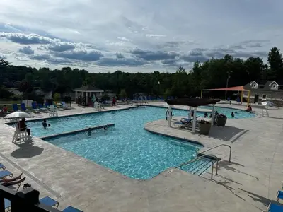 a large swimming pool with people sitting around it at Evergreen Villa Poconos - Hot Tub, Fire Pit, Close to Kalahari, Great Wolf Lodge and Camelback in Tobyhanna