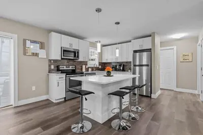 a kitchen with white cabinets and a island with bar stools at Evergreen Villa Poconos - Hot Tub, Fire Pit, Close to Kalahari, Great Wolf Lodge and Camelback in Tobyhanna