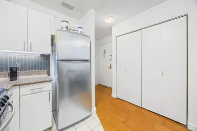 a stainless steel refrigerator in a kitchen with white cabinets at Chelsea 1BR in Shared Apt with Laundry and Rooftop in New York