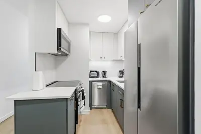 a kitchen with white cabinets and a stainless steel refrigerator at A Modern 1BR Oasis in Carriage House in Philadelphia