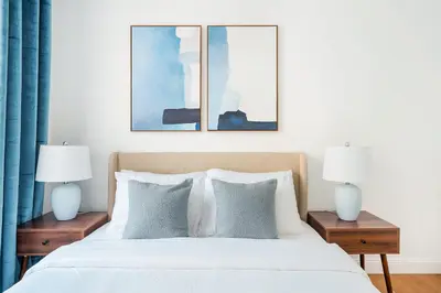 a bedroom with a bed with two lamps and three paintings at 26A-2 Spacious brand new Fully Furnished 2-Bedroom in Prime Murray Hill Move-In Ready in New York