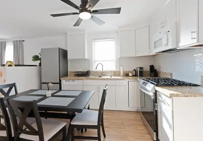 a white kitchen with a table and a ceiling fan at 17m to NYC,5 min to American Dream,2Parking Spaces in Carlstadt