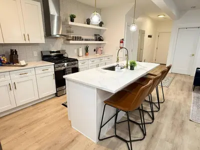 a kitchen with white cabinets and a kitchen island with bar stools at Modern 3BR Home | Chic & Cozy | 30 Min NYC Access in Jersey City