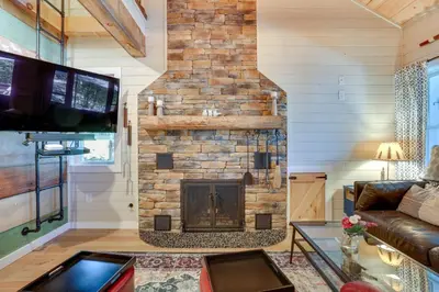a living room with a stone fireplace with a tv at Lakefront Cottage with Dock, Hot Tub and Fire Pit in Greentown