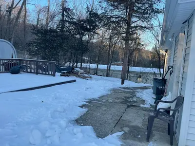 a yard covered in snow with a chair next to a house at Cheerful two bedroom bungalow near Mountain Creek in West Milford