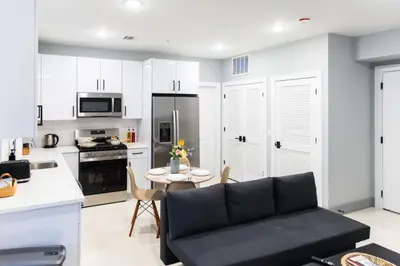 a living room with a black couch and a kitchen at 20 Minutes to Times Square, Stylish 2 Bedroom Apartment in West New York