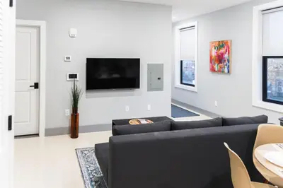 a living room with a couch and a tv on a wall at 20 Minutes to Times Square, Stylish 2 Bedroom Apartment in West New York