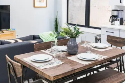 a wooden table with plates and glasses on it in a living room at 20 Minutes to Times Square with Free Indoor Parking in West New York