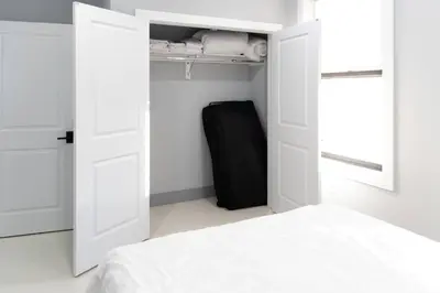 a white bedroom with a bed and a black suitcase at 20 Minutes to Times Square with Free Indoor Parking in West New York