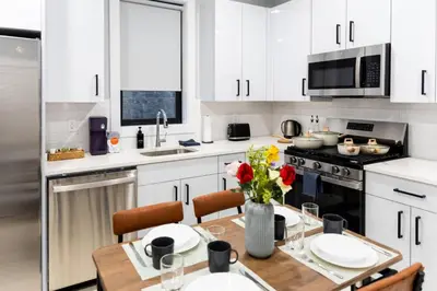 a kitchen with white cabinets and a wooden table with flowers at Quick NYC Access with Free Parking Two Bedrooms Near NYC in West New York