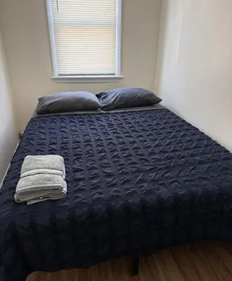 a bed with a blue comforter and a window at Private one-bedroom and one-bathroom apartment, private street entrance in convenient area, MetLife Stadium FIFA World Cup 35 minutes away in Perth Amboy
