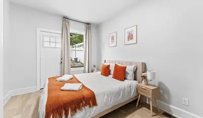 a white bedroom with a large bed with orange pillows at Chic 3BR-4BD-3Bath Oasis with Backyard Near NYC in Jersey City