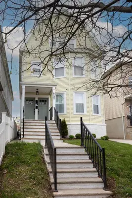 a yellow house with stairs in front of it at Excellence by Urooms Apartments Near NYC and Newark Airport with Parking in Elizabeth