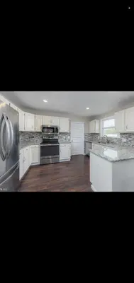 a kitchen with white cabinets and a stainless steel refrigerator at The Carneys Point Cottage