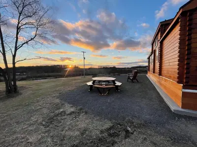 a picnic table next to a building with the sunset at Private Luxury Log Cabin in the Endless Mountains, Firepit, Farm Charm in Kingsley