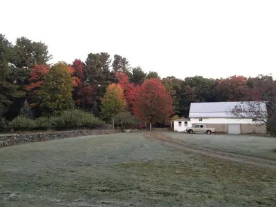 a barn with a car parked in front of a field at Apple Orchard & Forest Retreat with Woodland Pond in Forestburgh