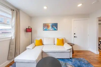 a living room with a white couch and yellow pillows at Modern 2BR 8 mins to Penn Station with WiFi Laundry in Newark