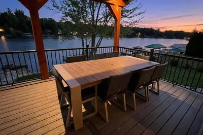 a wooden deck with a table and chairs on the water at 9 BR,34 Sleeps Skiing Lake Sauna Hottub Kayaks in Lake Harmony