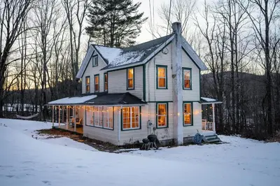 a house in the snow with lights on at The Swiss Hill Farmhouse - 5 Bedrooms w Hot Tub in Jeffersonville