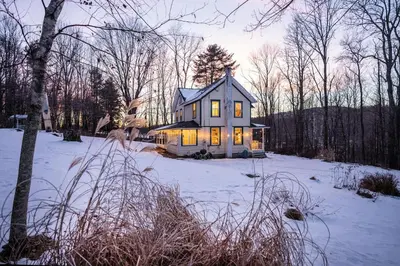 a house with its lights on in the snow at The Swiss Hill Farmhouse - 5 Bedrooms w Hot Tub in Jeffersonville