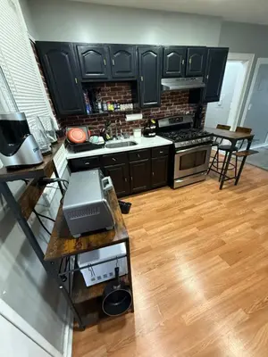 a kitchen with black cabinets and a wooden floor at EWRBNB - Rare Find! Huge 3BR Apartment with Open Layout minutes from Newark Airport & NYC - Apartment # 2 in Elizabeth