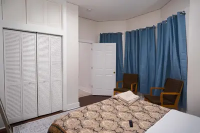 a bedroom with a bed and two chairs and blue curtains at Stylish & Comfortable City Stay in West New York